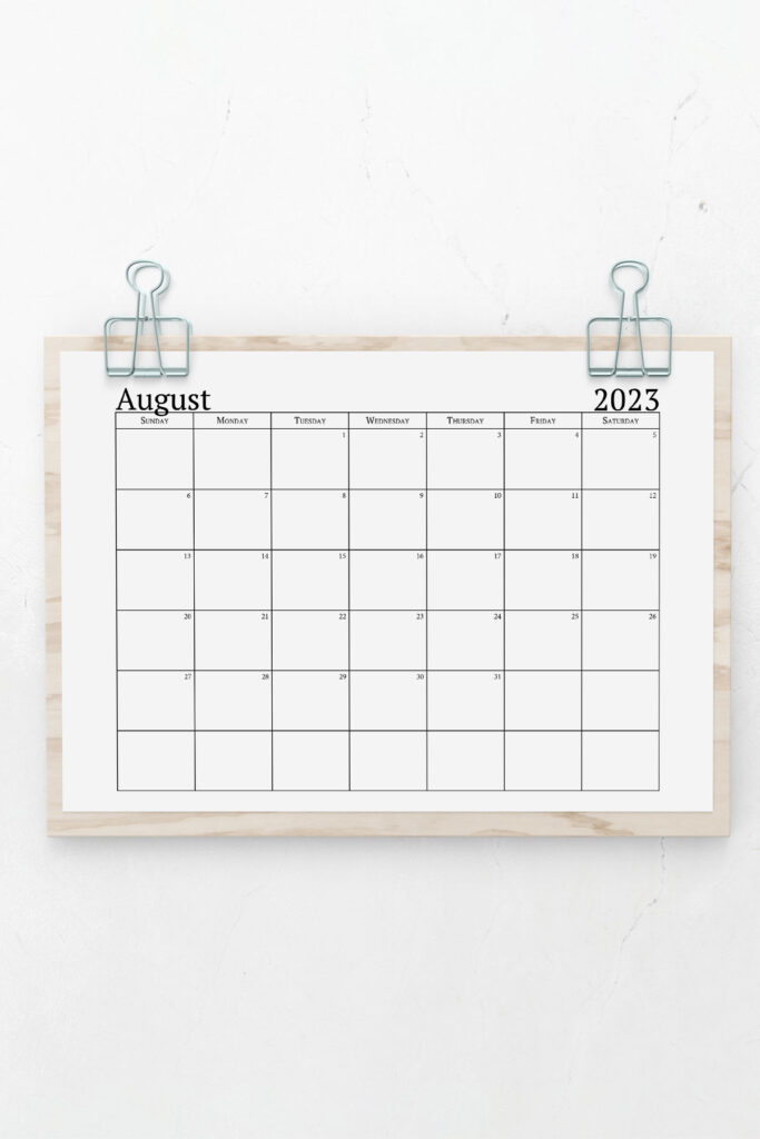 This image shows a 2023 printable calendar one page design hanging by silver binder clips. This is an example of a portion of the 2023 yearly calendar you can get for free at the end of this post. This is showing the month of August 2023 in a simple black text.