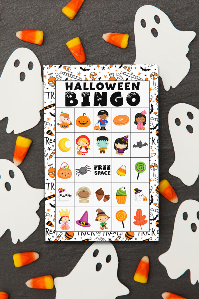 The image shows one of the 40 unique Halloween bingo cards you can get for free at the end of this blog post. The top of the card says Halloween Bingo. Below it are various Halloween images such as pumpkins, Halloween treats, and more. Surrounding the Halloween Bingo printable are white paper ghosts and some candy corn.