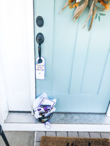 This image shows the you’ve been booed door hanger you can get for free in the You’ve been Booed printable set at the end of this blog post. It’s a white door hanger with a purple outline. It has a little ghost and says, “You’ve been booed!” It also includes a little boo basket sitting on the door frame. The book basket is filled with Halloween treats and trinkets. It has a little gift tag that says “You’ve Been Booed.”