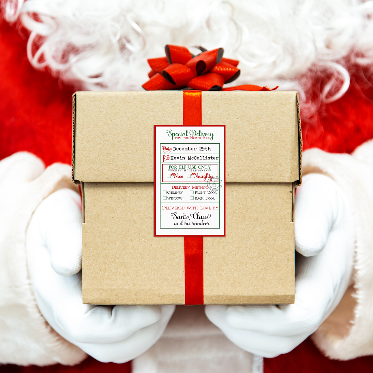 The image shows one of the tags from the Christmas tags from Santa printable set. The tag is on a package wrapped with Kraft wrapping paper and a red bow and is being held by hands that appear to be Santa’s hands.