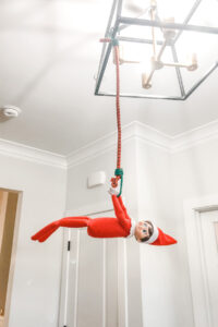 This image shows an elf on the shelf hanging by a bungee cord off of a light fixture. This is one of the many elf on the shelf ideas for home included in this post. Check out this list of over 50 Elf on the Shelf ideas for home including this elf hanging from a light by a bungee cord. There are tons of easy ideas, funny ideas, last minute ideas, and more. Plus, you’ll get a set of free Elf on the Shelf planning printables. This includes a blank elf on the shelf calendar, list of elf on the shelf ideas, printable elf on the shelf notes, a fillable elf on the shelf note set, and more.