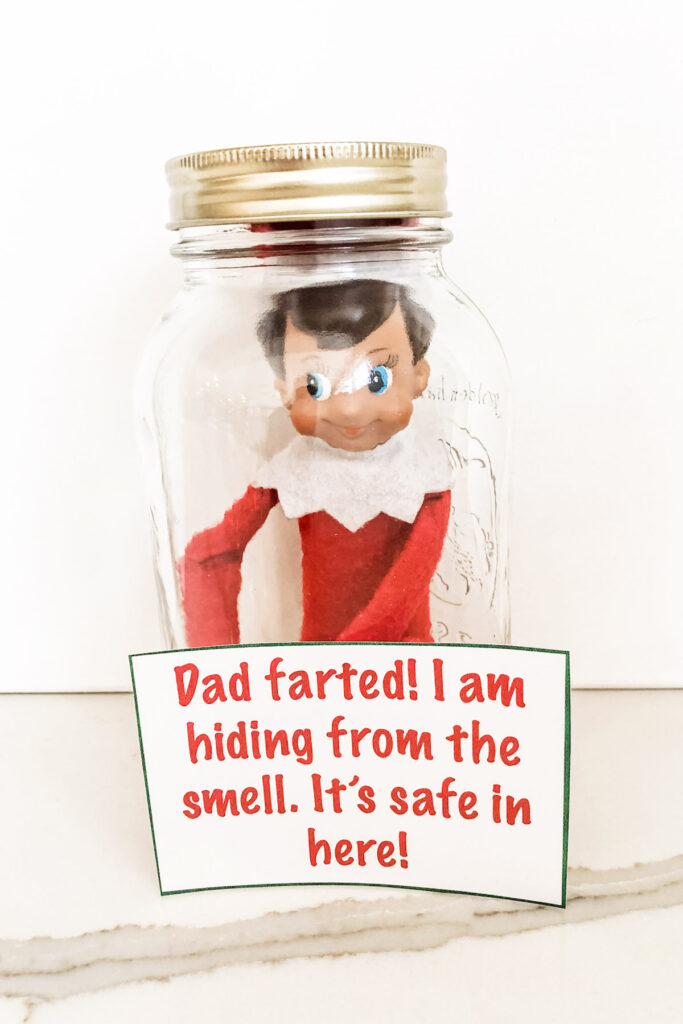 This image shows the elf on a shelf doll inside of a glass mason jar with the lid on it. There is a note that says Dad farted! I am hiding fro the smell. It’s safe in here! This is one of the many elf on the shelf ideas for home included in this post.