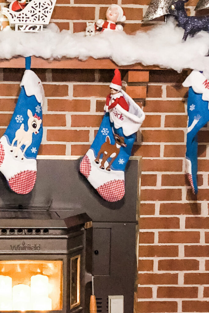 In this image an elf is inside of a stocking. This is one of the many elf on the shelf ideas for home included in this post.