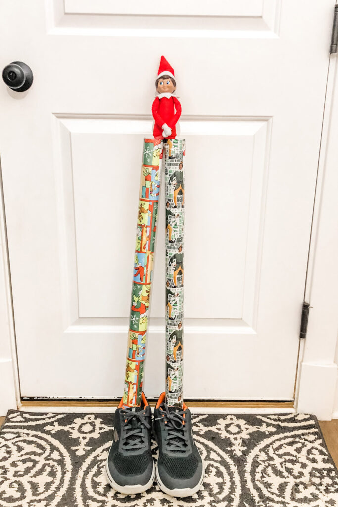 There is an elf with each one of his legs stuck into a roll of wrapping paper. The wrapping paper is stuck inside a pair of men’s shoes. So it is like he is standing up and his legs are wrapping paper tubes. This is one of the many elf on the shelf ideas for home included in this post.
