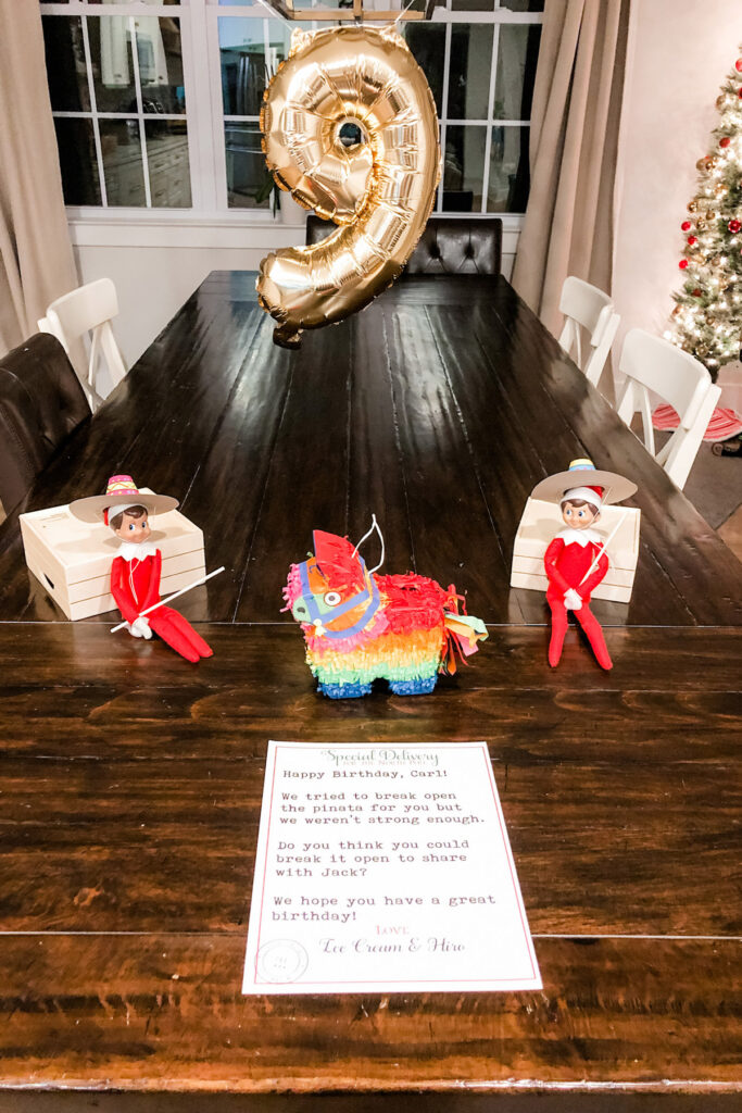 This image shows two elves wearing sombreros holding sticks and a mini piñata with a number 9 balloon. This is one of the many elf on the shelf ideas for home included in this post.