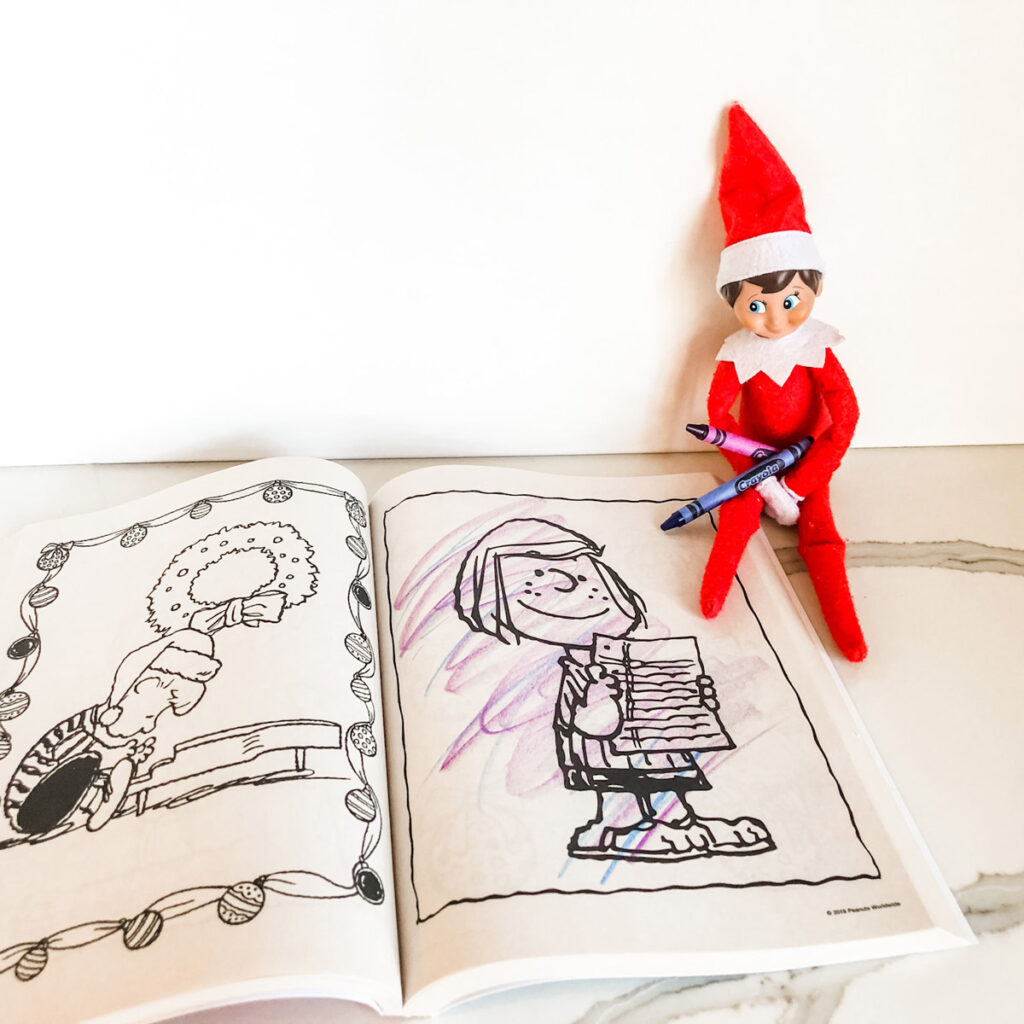 This image shows an elf on the shelf with crayons in his hand. Below that is a coloring book that has been scribbled all over. This is one of the many elf on the shelf ideas for home included in this post.