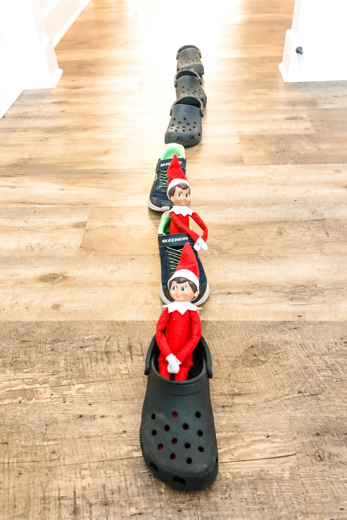 This image shows 2 elf on a shelf dolls in shoes that are lined up like a train. This is one of the many elf on the shelf ideas for home included in this post.