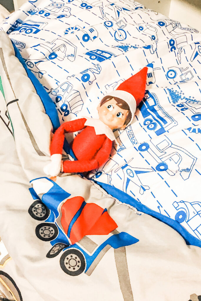 This image shows an elf on the shelf doll laying in a bed. This is one of the many elf on the shelf ideas for home included in this post.