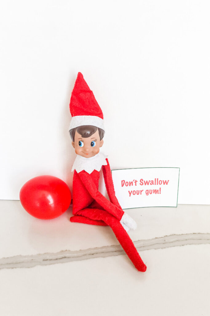 This image shows an elf on the shelf with a balloon sticking out of his butt. There is a note that says, don’t swallow your gum! This is one of the many elf on the shelf ideas for home included in this post.