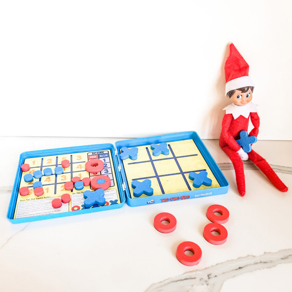 This image shows an elf on the shelf playing tic tac toe. This is one of the many elf on the shelf ideas for home included in this post.