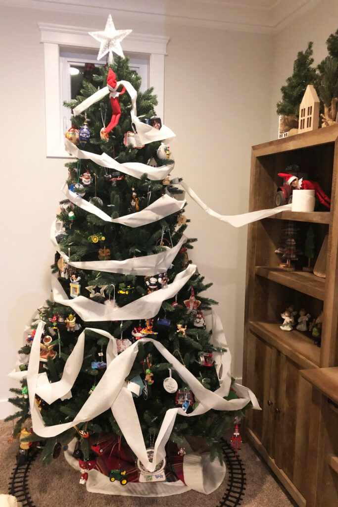 In this image, 2 elf on the shelf dolls have toilet papered a Christmas tree. This is one of the many elf on the shelf ideas for home included in this post.