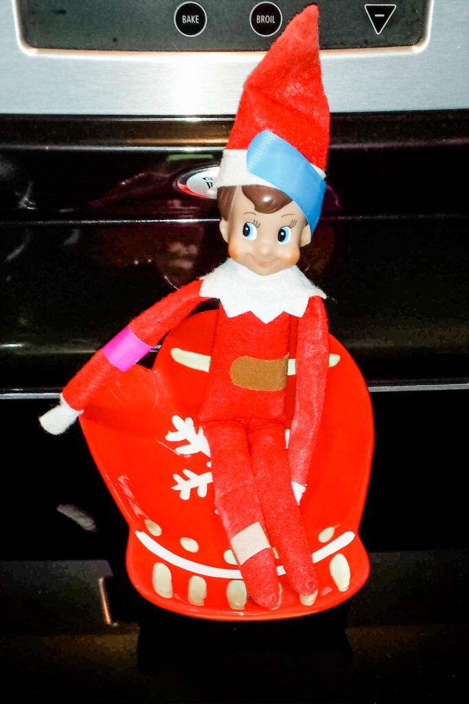 In this image, an elf on the shelf doll is covered in bandaids. This is one of the many elf on the shelf ideas for home included in this post.