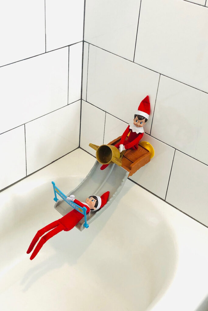 In this image, there are 2 elf on a shelf dolls playing on a bath toy. This is one of the many elf on the shelf ideas for home included in this post.