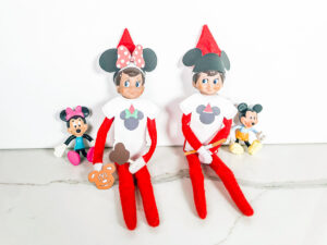 This image shows two Elf on the Shelf dolls wearing their free Elf on the Shelf Mouse Ears and Snacks printable items that you can get for free at the end of this blog post.