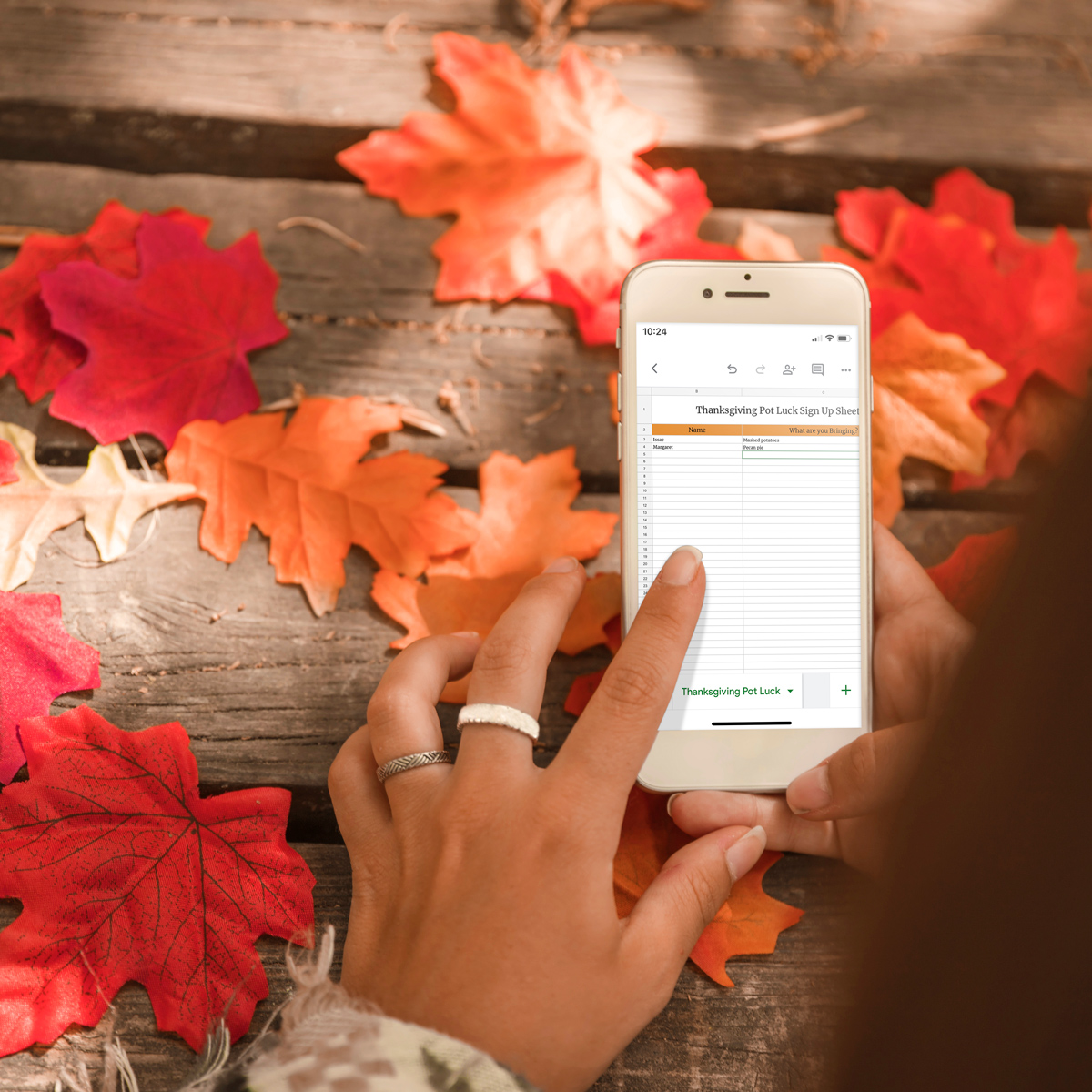 This image is showing an example of one of the available sign up sheets included in the free printable and digital Thanksgiving potluck sign up sheets. This is an example of one of the digital options - it shows a phone with the screen showing one of the Thanksgiving Pot Luck Sign Up Sheet Google sheet.