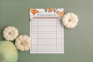This image shows Thanksgiving shopping list you can get as part of the Thanksgiving shopping list printable, to do lists, and menu planner set at the end of this blog post. This image shows the shopping list surrounded by some pumpkins.
