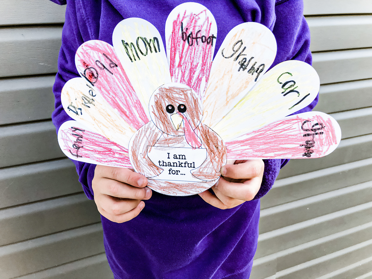 This is an image of a boy holding up his competed free Thanksgiving thankful turkey printable you can get for free at the end of this blog post.