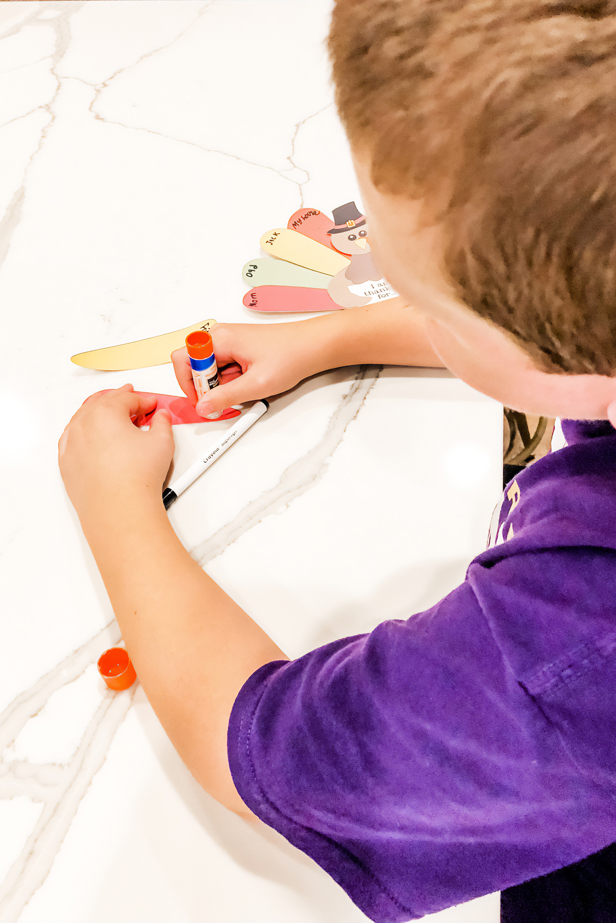 This is an image of a boy gluing together the free Thanksgiving thankful turkey printable you can get for free at the end of this blog post.