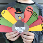 This is an image of a boy holding up his competed free Thanksgiving thankful turkey printable you can get for free at the end of this blog post.