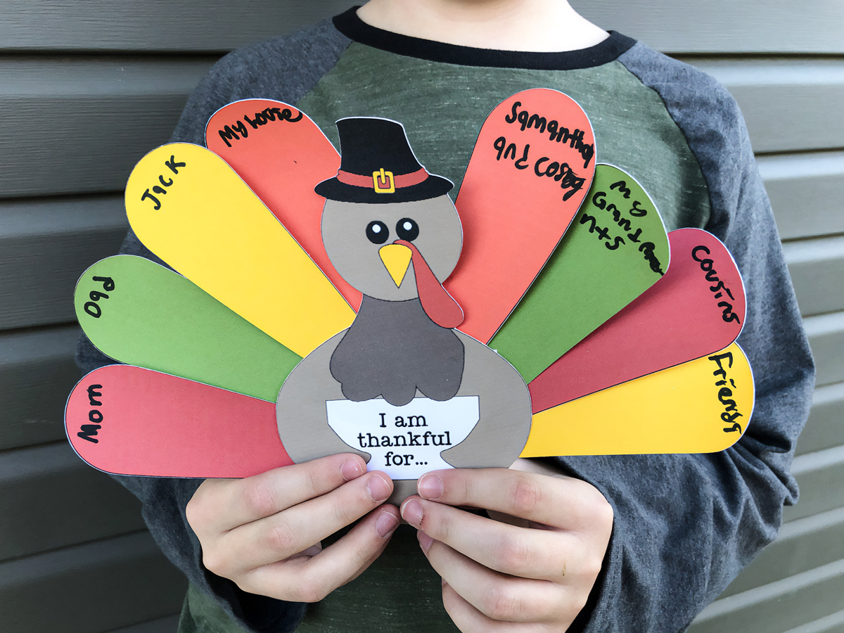 This is an image of a boy holding up his competed free Thanksgiving thankful turkey printable you can get for free at the end of this blog post.