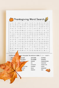 This image shows a Thanksgiving Word search printable which you can get at the end of the blog post. At the top of the word search, it says Thanksgiving word search. Below that is a grid of letters. Underneath that is a list of Thanksgiving themed words to search for (such as turkey, rolls, football, and more). This example also has color Thanksgiving clip art including a pumpkin, ear of corn, acorn, and slice of pumpkin pie. On top of the paper is a left in the bottom left corner.