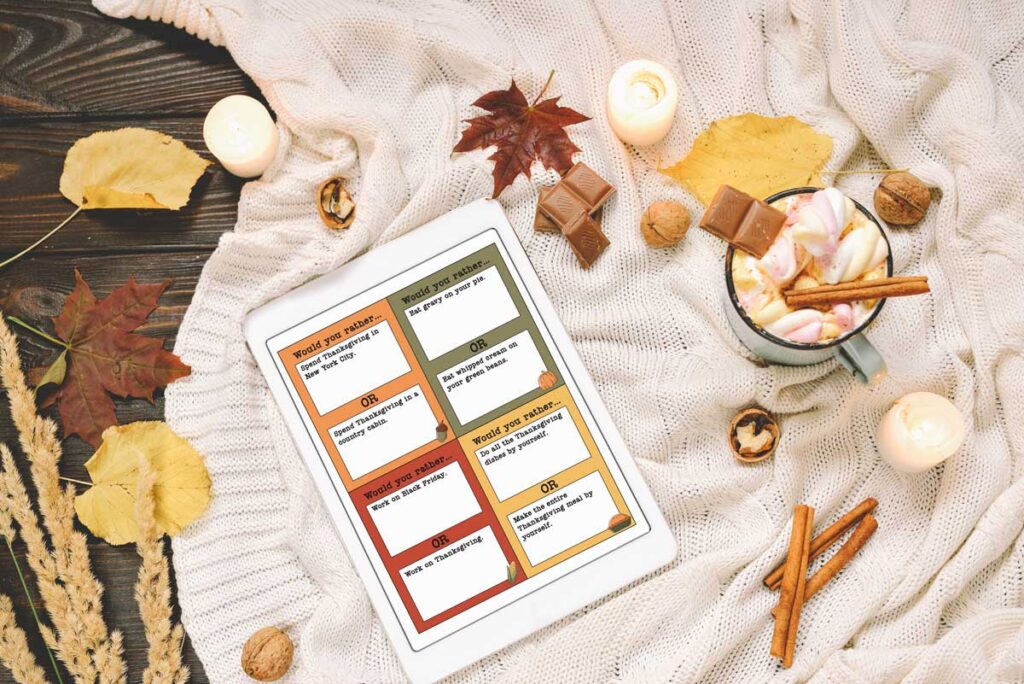 This image shows one of the sheets available to download from the would you rather Thanksgiving games printable. There are 20 questions included on 5 pages and this is one of the pages represented on an ipad. The iPad is sitting on a blanket surrounded by fall decor and a mug with a drink.