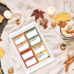 This image shows one of the sheets available to download from the would you rather Thanksgiving games printable. There are 20 questions included on 5 pages and this is one of the pages represented on an ipad. The iPad is sitting on a blanket surrounded by fall decor and a mug with a drink.