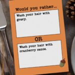 This image shows one of the question cards from the Would you Rather Thanksgiving games printable. There are twenty Thanksgiving would you rather question cards included in this free set you can get in this blog post. This question says, would you rather wash your hair with gravy or wash your hair with cranberry sauce. The card is sitting on a table surrounded by pumpkins, pinecones, wheat stalks, silverware, and a plate.