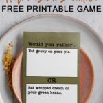 At the top, it says would you rather Thanksgiving edition free printable game. Below that is an image that shows one of the question cards from the Would you Rather Thanksgiving games printable. There are twenty Thanksgiving would you rather question cards included in this free set you can get in this blog post. This question says, would you rather eat gravy on your pie or eat whipped cream on your green beans. The card is sitting on a plate.