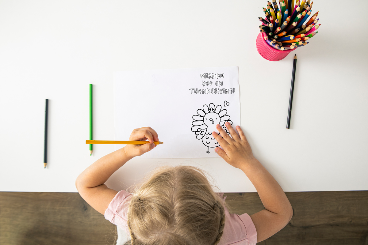 This image shows a little girl coloring one of the cards from the thanksgiving cards coloring pages set. It says missing you on thanksgiving. Below that is an image of a turkey and a heart.