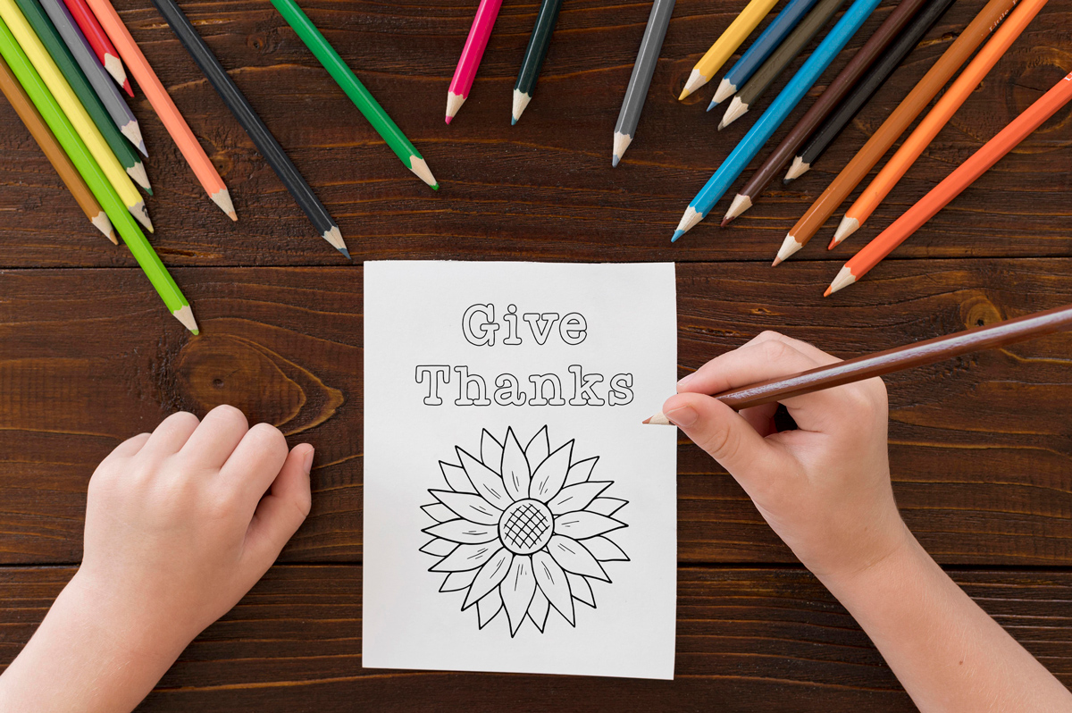 The image shows a child holding a coloring pencil about to color one of the cards from the thanksgiving cards coloring pages set. It says gives thanks. Below that is a drawing of a sunflower.