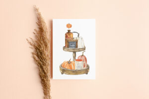 This image shows one of the free Thanksgiving cards you can get from the thanksgiving cards printable set. This card has a wood tiered tray drawing with some fall items including a sign that says grateful, thankful blessed, and a mug that says hello pumpkin. It is surrounded by a stalk of wheat.