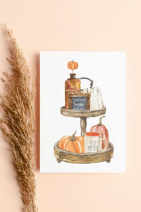 This image shows one of the free Thanksgiving cards you can get from the thanksgiving cards printable set. This card has a wood tiered tray drawing with some fall items including a sign that says grateful, thankful blessed, and a mug that says hello pumpkin. It is surrounded by a stalk of wheat.