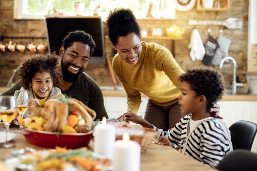 This image shows a family sitting around a Thanksgiving dinner table laughing.