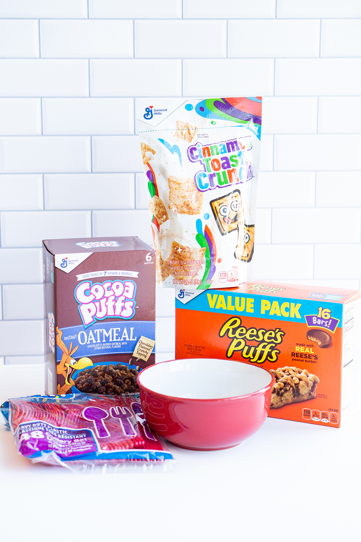 This image shows the materials you need to make the DIY I love you cerealsly bowl. It includes cereal, cereal themed oatmeal, cereal bars, a red bowl, and red silverware.