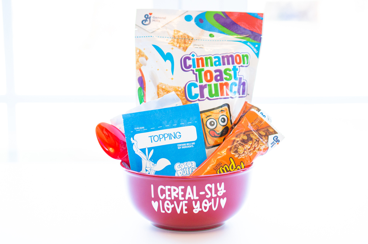 This image shows the I cerealsly love you SVG applied to a red cereal bowl. The bowl has a bag of cereal, two cereal bars, a bag of oatmeal, and a red spoon sitting inside of it.