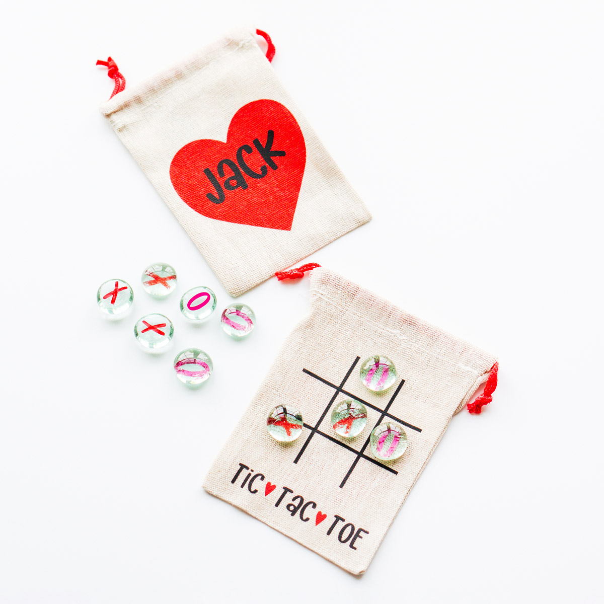 This image is showing the Valentine tic tac toe SVG you can get for free in this blog post. It is being showed on a small brown canvas bag and with small little clear gems that say x and on on them. There is also a name on the front it says Jack. The back shows a tic tac toe board with the words tic tac toe at the bottom.