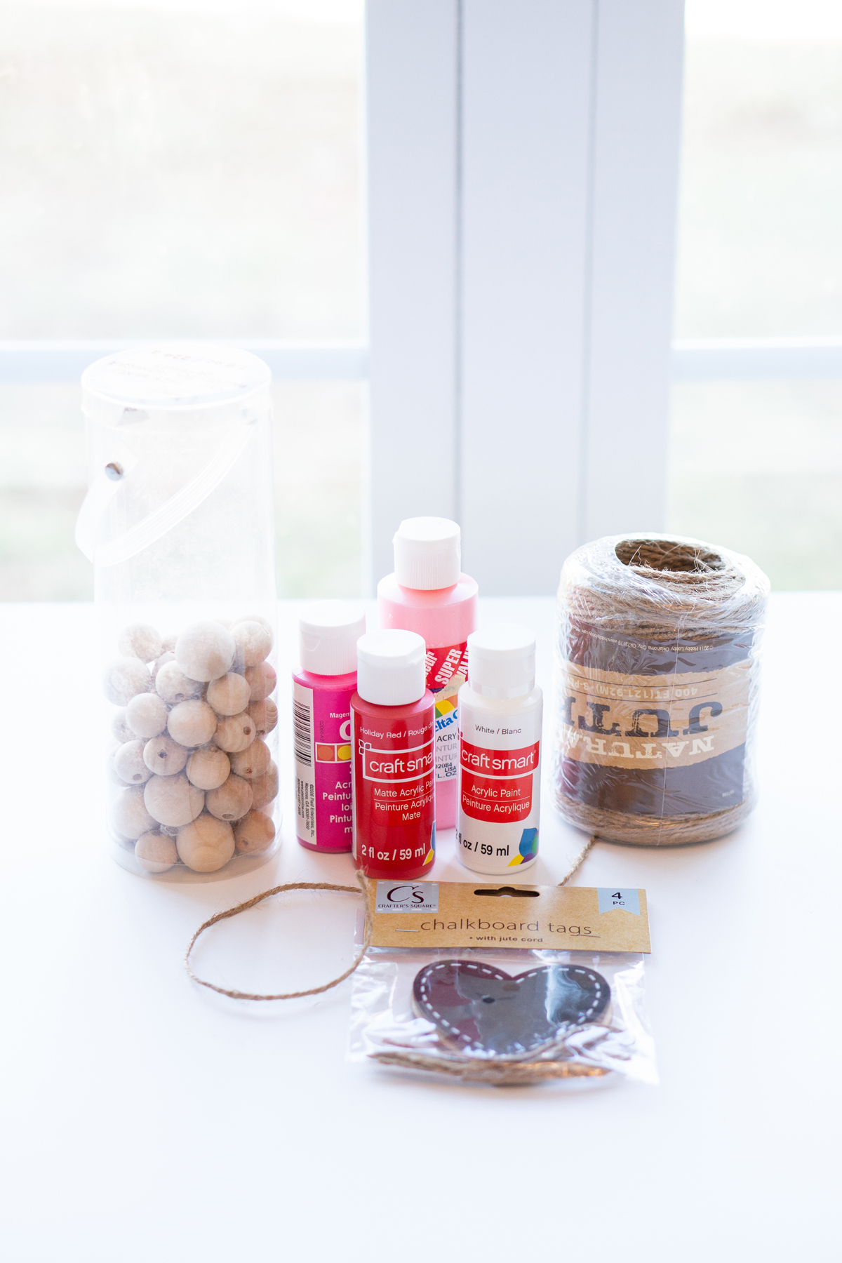 This image shows the materials needed to make DIY Valentine wood beads. It shows wood beads, paint, jute twine, and wood heart cut outs.