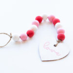 This image shows the final DIY Valentine wood beads with a wood heart painted in white that says love in cursive in pink on it.