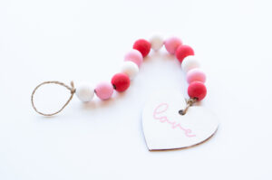 This image shows the final DIY Valentine wood beads with a wood heart painted in white that says love in cursive in pink on it.
