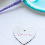 This image says the word love in pink on a white painted wood heart.