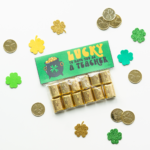 This image shows a completed free lucky to have you gift. It says on it, lucky to have you as a teacher. It is attached to a bag filled with Hershey's Nuggets. It is surrounded by plastic gold coins and four leaf clover cut outs.
