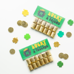 This image shows 2 completed free lucky to have you gifts. It says on it, lucky to have you as a friend on one and lucky to have you as a teacher on the other. Each topper is attached to a bag filled with Hershey's Nuggets. They are surrounded by plastic gold coins and four leaf clover cut outs.