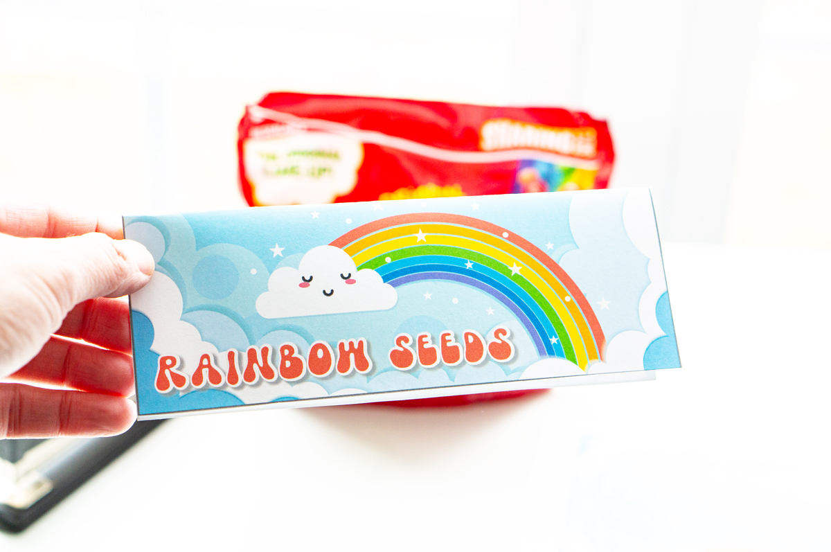 There is a bag topper being held that says Rainbow Seeds and has a picture of a rainbow.