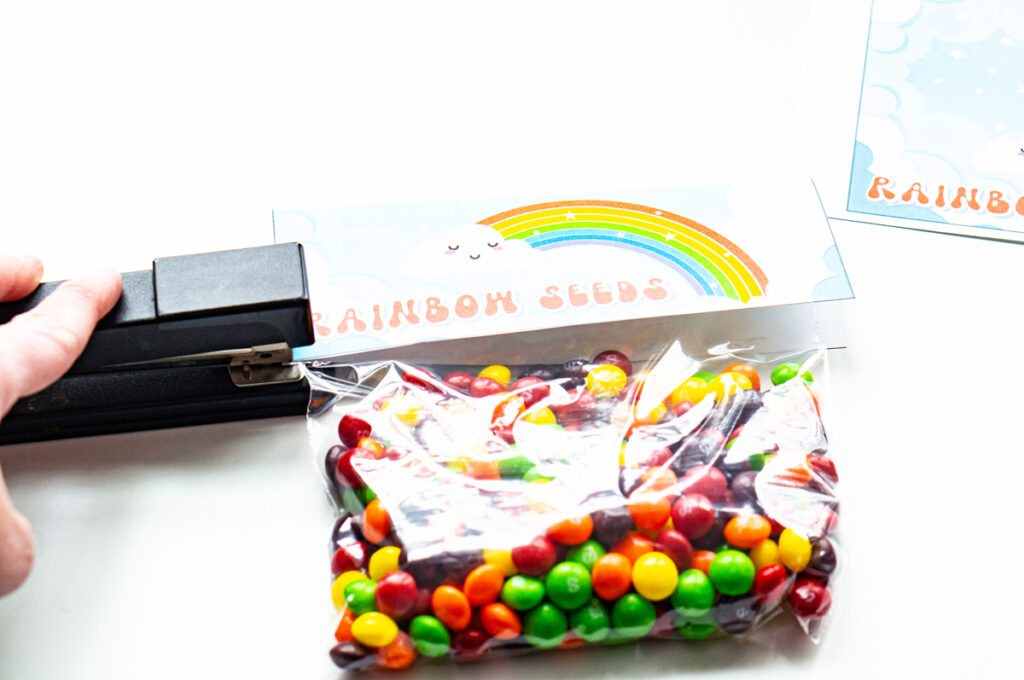 This image shows stapling a bag topper on top of a bag of skittles. The bag topper says rainbow seeds.