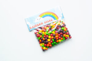 This image shows a bag of skittles with a bag topper that says rainbow seeds on it with a picture of a rainbow.