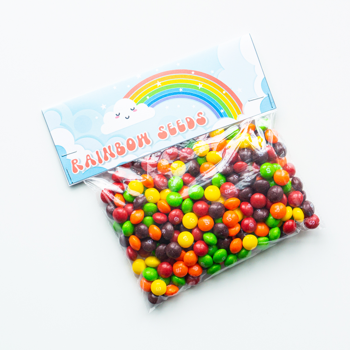 This image shows a bag of skittles with a bag topper that says rainbow seeds on it with a picture of a rainbow.