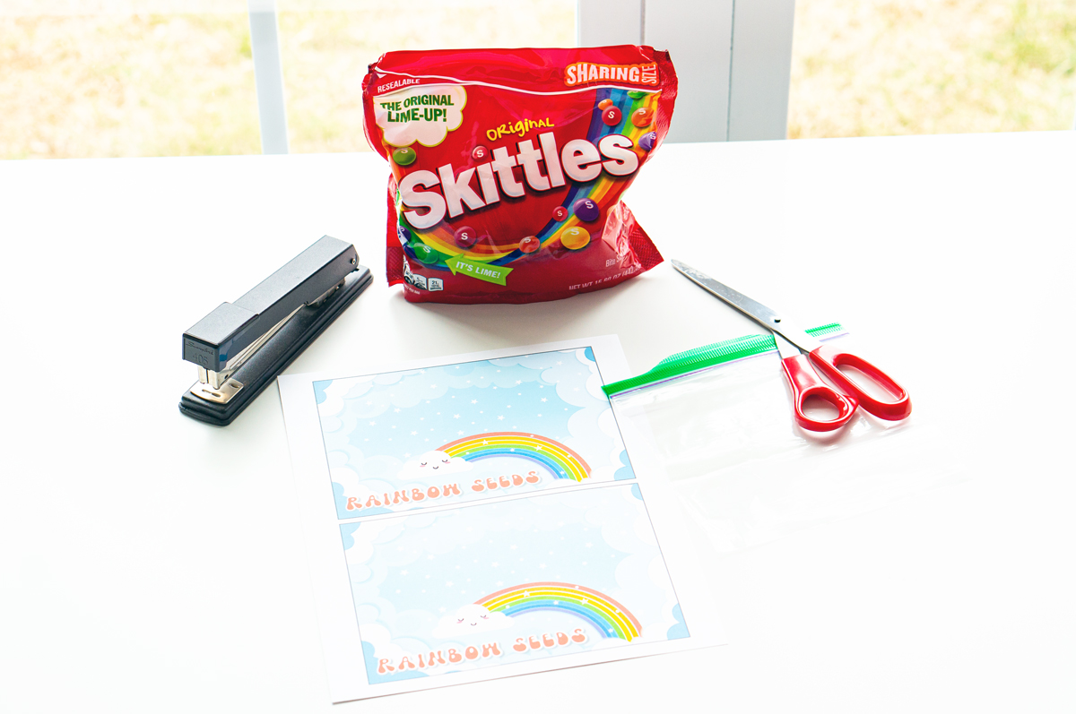 This image shows the materials needed to create your own rainbow seeds bag - stapler, rainbow seeds printable that you can get for free in this post, scissors, and plastic bag.