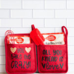 This image shows 2 pot holder baking gift sets. It has two pot holders - one says you bake me crazy with two cookies. The other says all you knead is love with two hearts. Each pot holder has a baking set and one has a whisk and the other has a spatula.