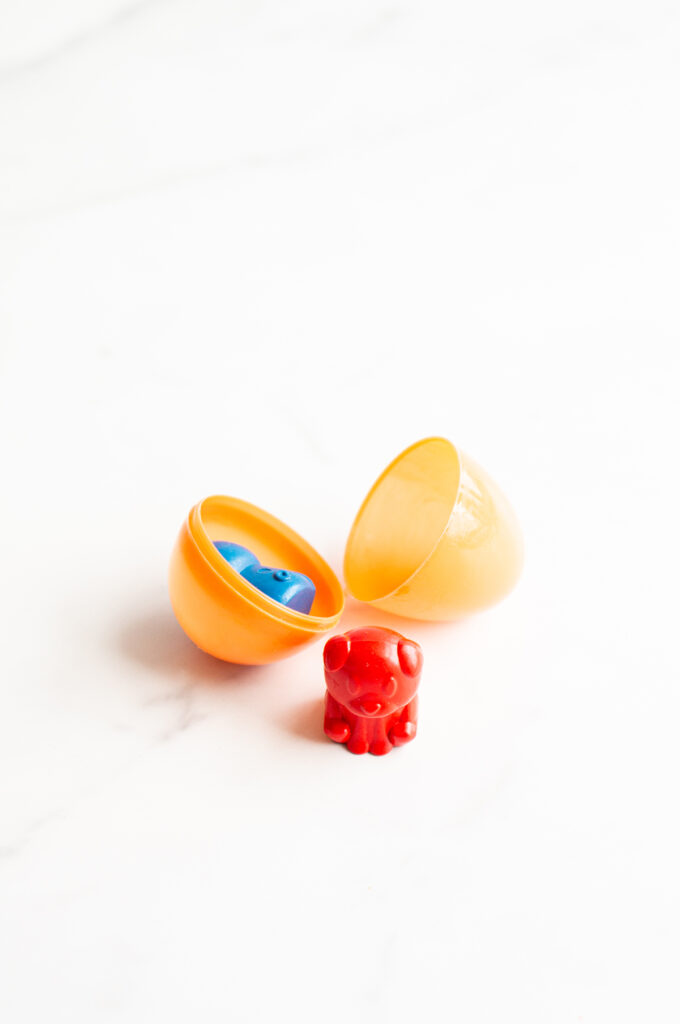 This image shows a plastic easter egg filled with non candy item of dog shaped crayons.